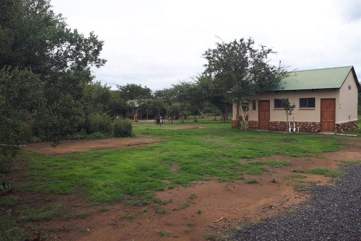 A view of the farm grounds featuring a single-story building with a green metal roof and stone base detailing, surrounded by natural landscape.