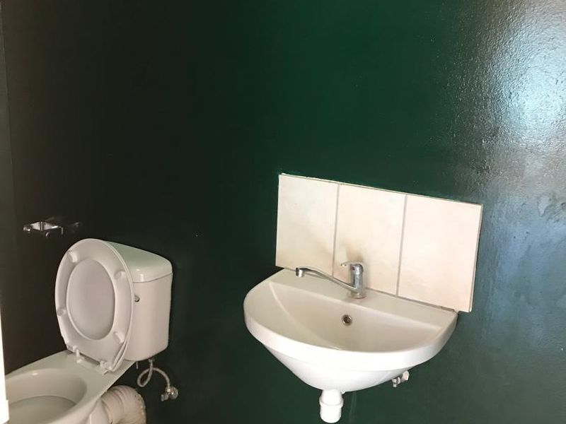 A small bathroom featuring a wall-mounted basin with a tiled splashback and a standard toilet, finished with dark green walls and tiled flooring.