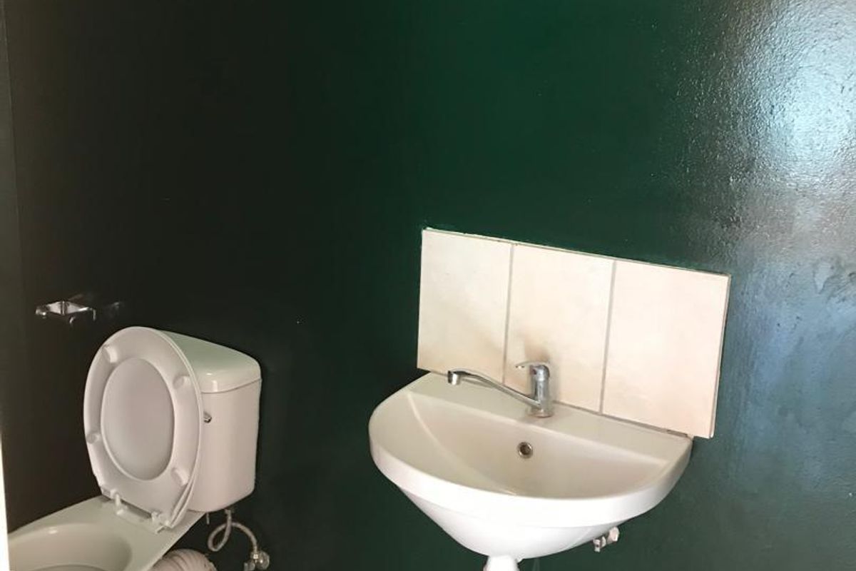 A small bathroom featuring a wall-mounted basin with a tiled splashback and a standard toilet, finished with dark green walls and tiled flooring.