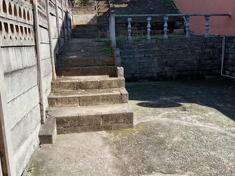 Rear exterior area featuring concrete stairs, a retaining wall, and a precast boundary wall, showing significant signs of weathering and wear.