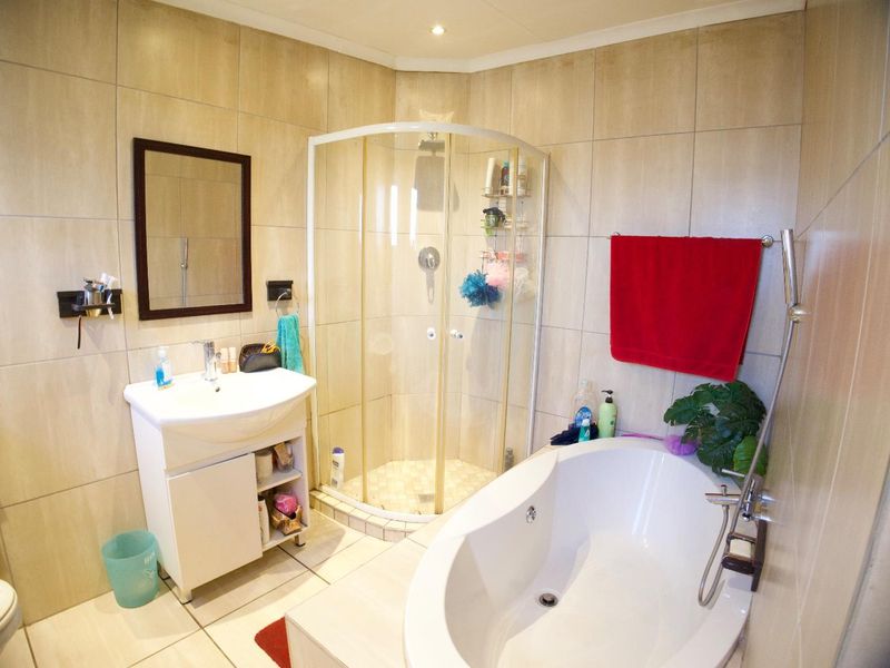 A functional bathroom featuring a corner shower enclosure, a modern freestanding bathtub, a vanity basin, and neutral floor-to-ceiling wall tiling.