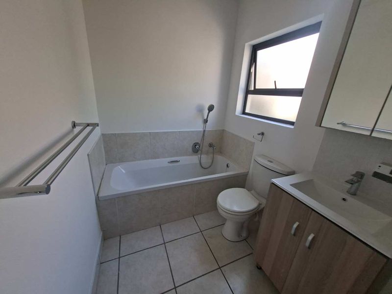 A clean and functional bathroom featuring a built-in bathtub with shower attachment, a vanity unit with basin, and tiled finishes.