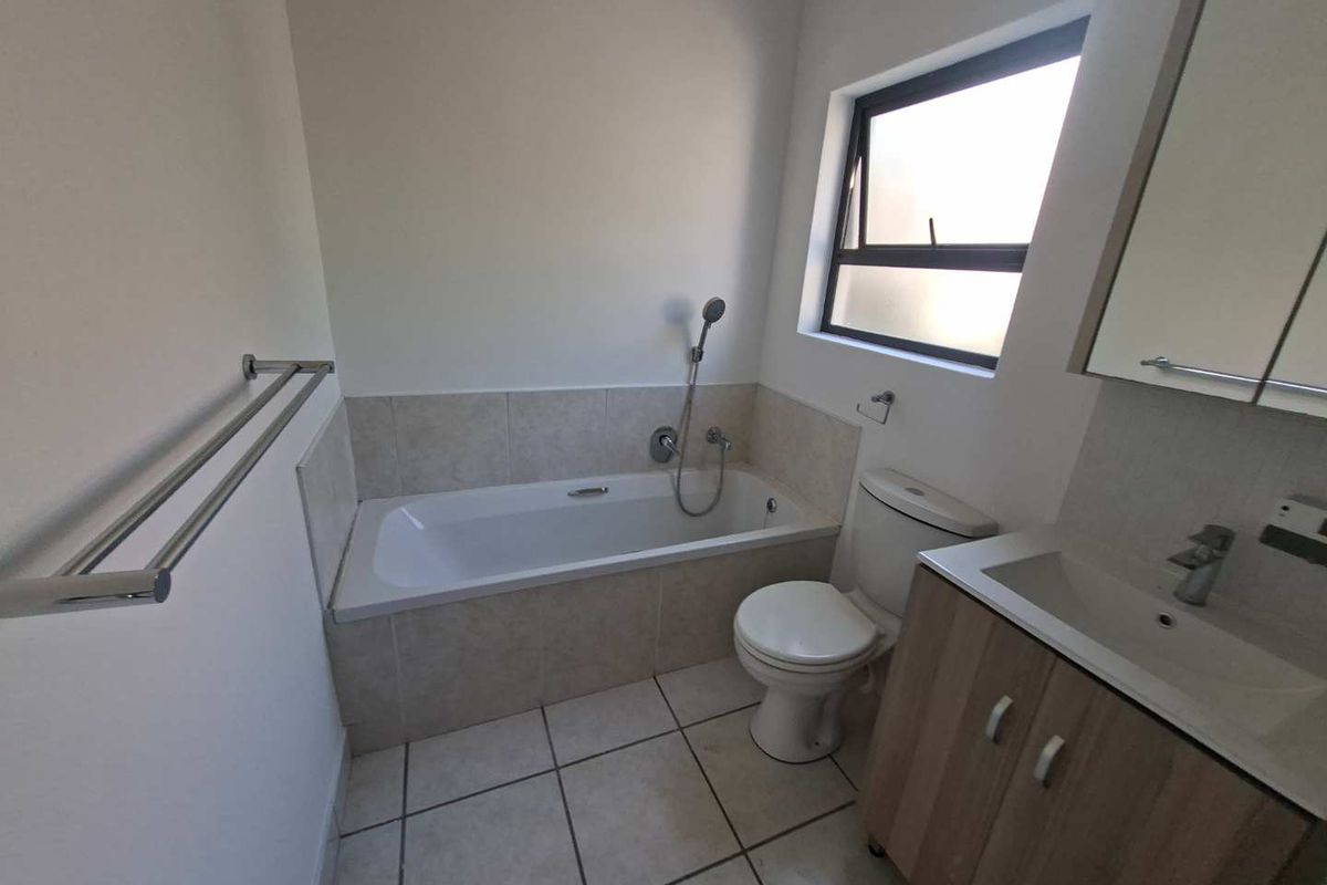A clean and functional bathroom featuring a built-in bathtub with shower attachment, a vanity unit with basin, and tiled finishes.