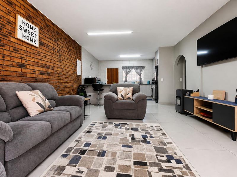 Open-plan living area featuring an exposed brick wall, tiled flooring, and a seamless transition into the kitchen space.