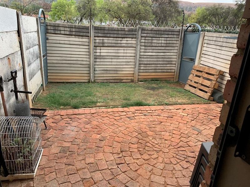 A private rear courtyard featuring a circular brick paved patio area and a small grass section enclosed by precast concrete walls with electric fencing.