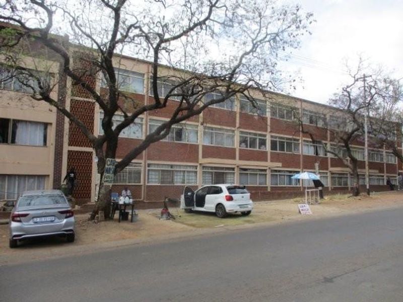 Street view of a multi-story apartment building featuring a brick facade and large windows, situated along a public road.