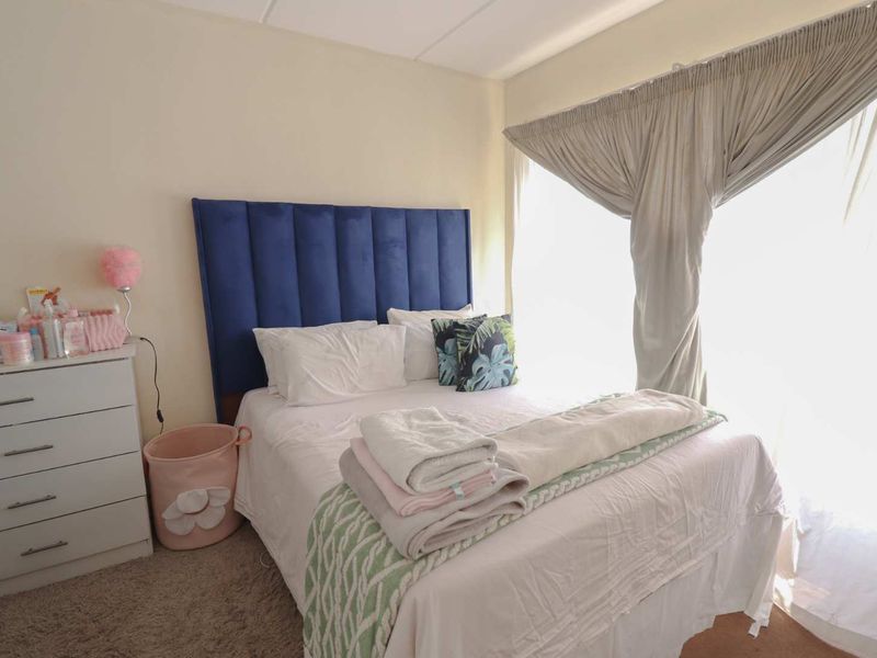 A bedroom featuring carpeted flooring and large windows with curtain tracks, providing natural light and a comfortable living space.