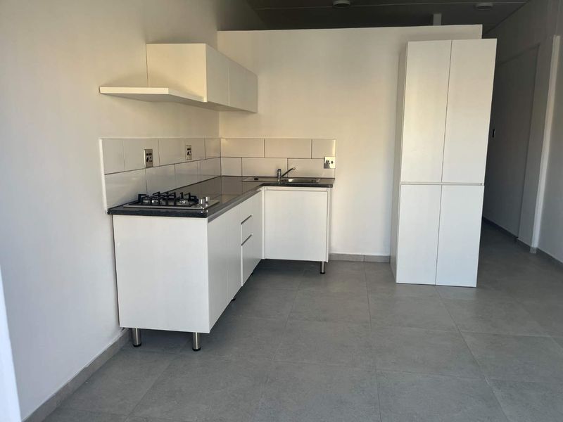 A clean, modern kitchen featuring white cabinetry, a gas hob, tiled backsplash, and neutral floor tiles in an open-plan layout.