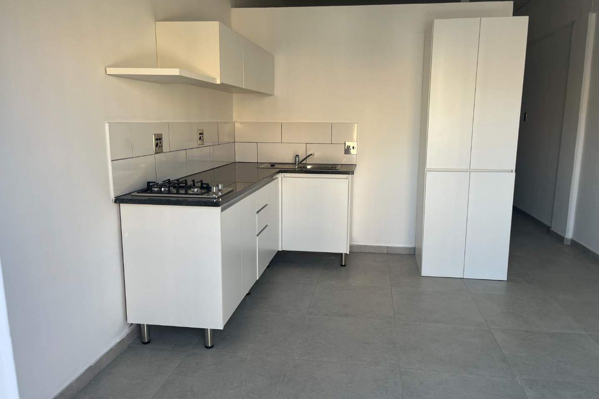 A clean, modern kitchen featuring white cabinetry, a gas hob, tiled backsplash, and neutral floor tiles in an open-plan layout.