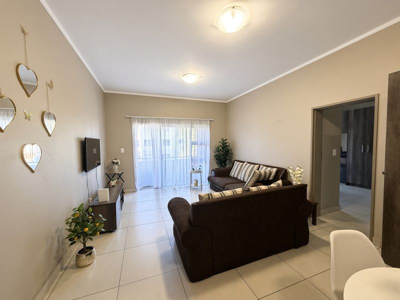 A well-maintained living room featuring neutral tiled flooring, ample natural light from a sliding glass door, and clean wall finishes.