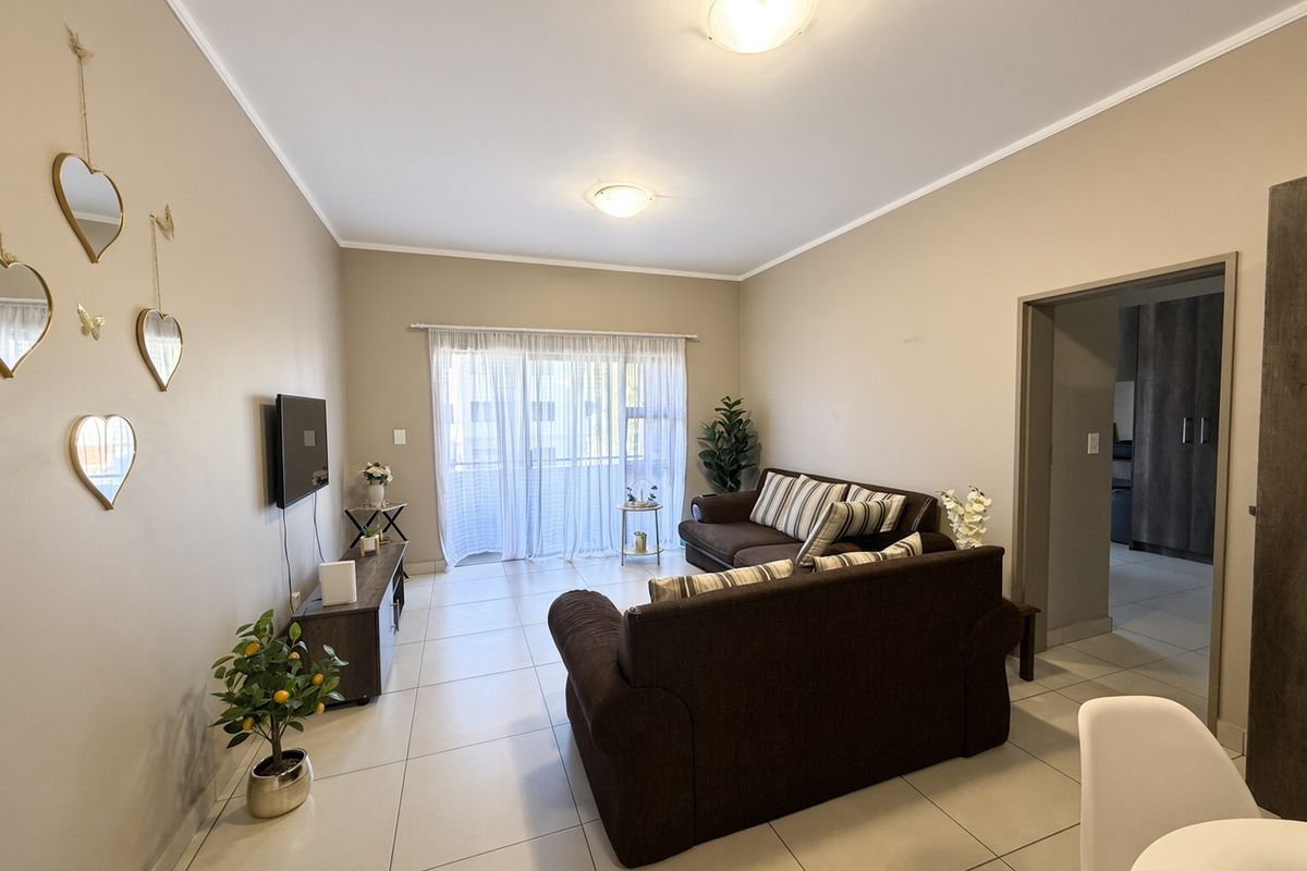 A well-maintained living room featuring neutral tiled flooring, ample natural light from a sliding glass door, and clean wall finishes.