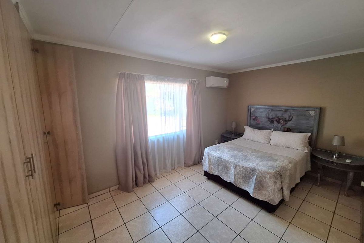 A bedroom featuring tiled flooring, built-in cupboards, and a wall-mounted air conditioning unit.