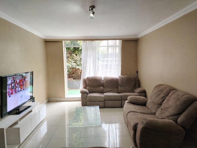 A living room featuring tiled flooring, ceiling cornice, and a sliding glass door providing natural light and garden access.