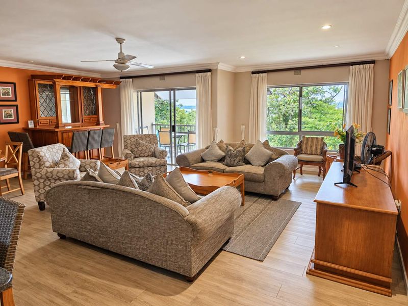 Spacious living room featuring laminate flooring, a built-in bar, ceiling fan, and large sliding glass doors that open to a balcony with scenic views.