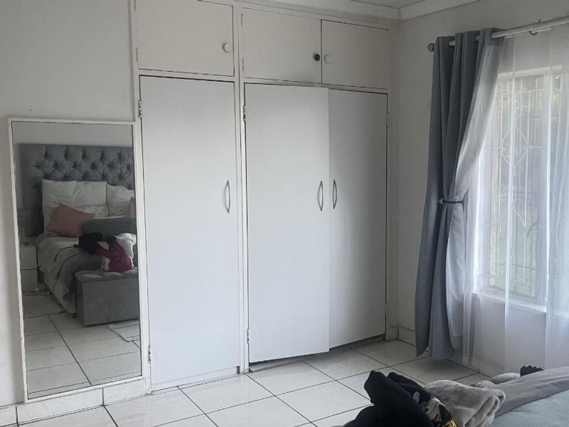 Bedroom featuring built-in cupboards, tiled flooring, and a window with security bars.