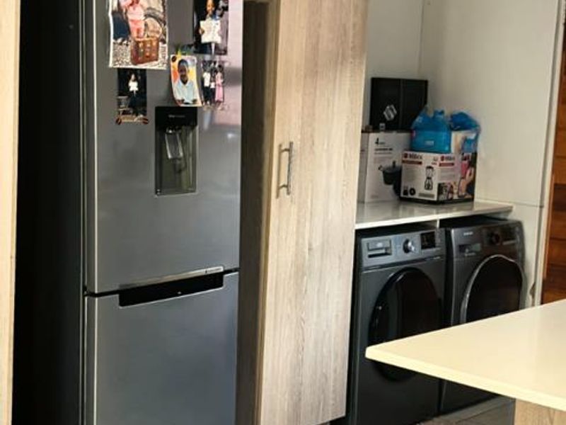 A functional kitchen area featuring light wood-grain built-in cabinetry, tiled flooring, and dedicated space for appliances.