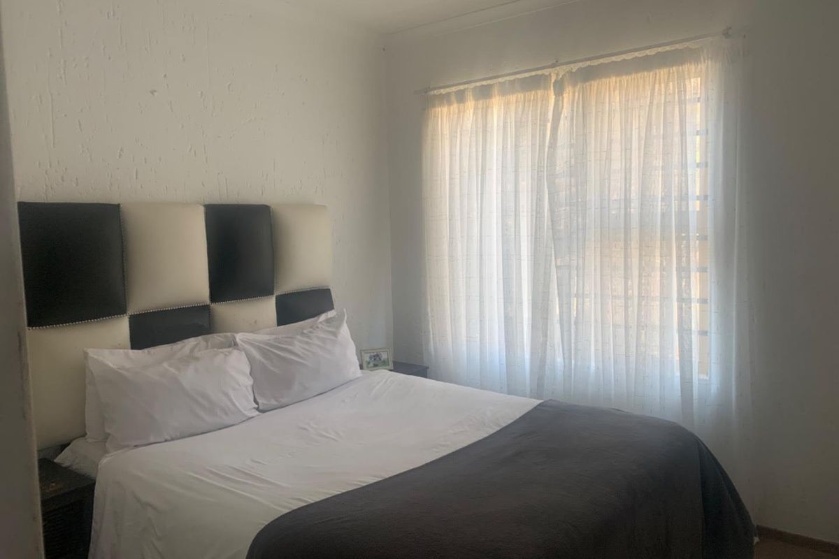 A bedroom featuring textured walls and a window with fitted security bars.