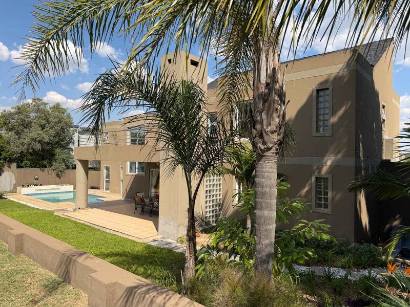 Rear view of a two-story house featuring a swimming pool, tiled patio area, balcony, and distinctive glass block window detailing.