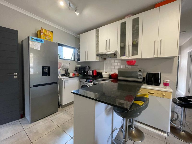 Compact kitchen featuring white cabinetry, granite countertops, a breakfast bar, and a subway tile backsplash with tiled flooring.