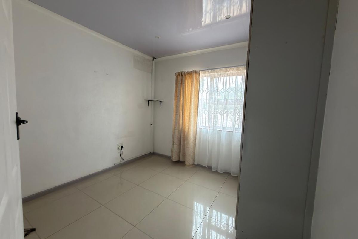 A vacant bedroom featuring tiled flooring, a built-in cupboard, and a security gate on the window, offering a clean canvas for personalization.