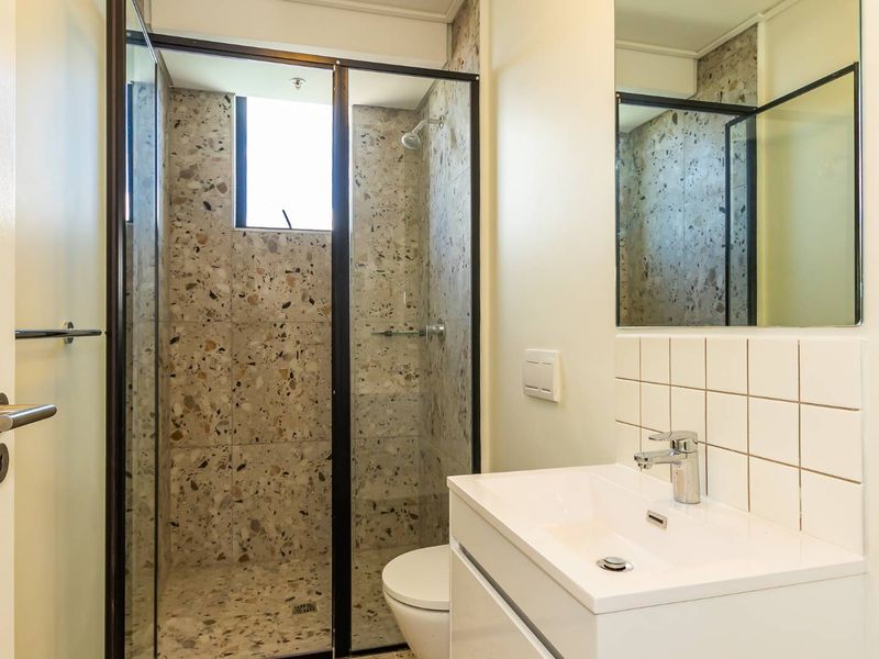 Modern bathroom featuring a glass-enclosed shower with terrazzo tiling, a sleek vanity basin with chrome fixtures, and a wall-mounted mirror.