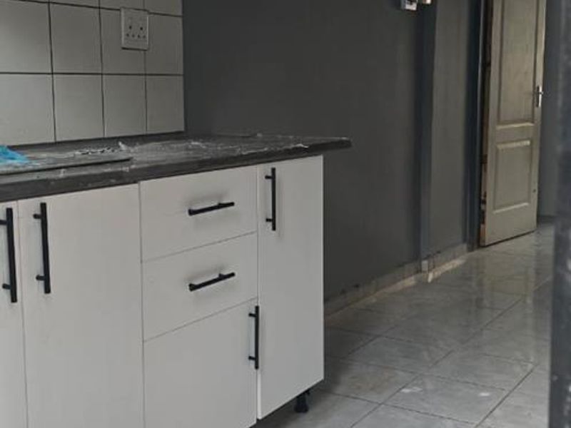 A compact kitchen featuring white cabinetry, tiled backsplash, and tiled flooring, presenting a clean and functional space ready for personalization.