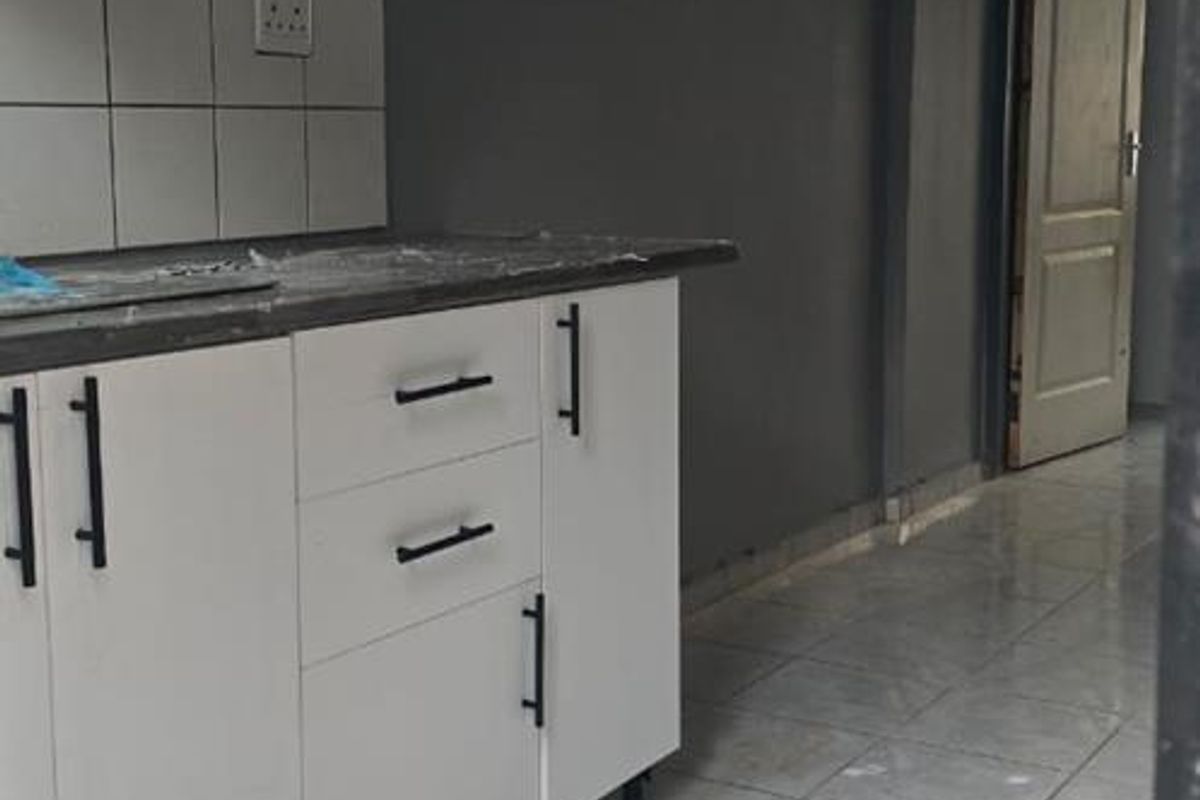 A compact kitchen featuring white cabinetry, tiled backsplash, and tiled flooring, presenting a clean and functional space ready for personalization.