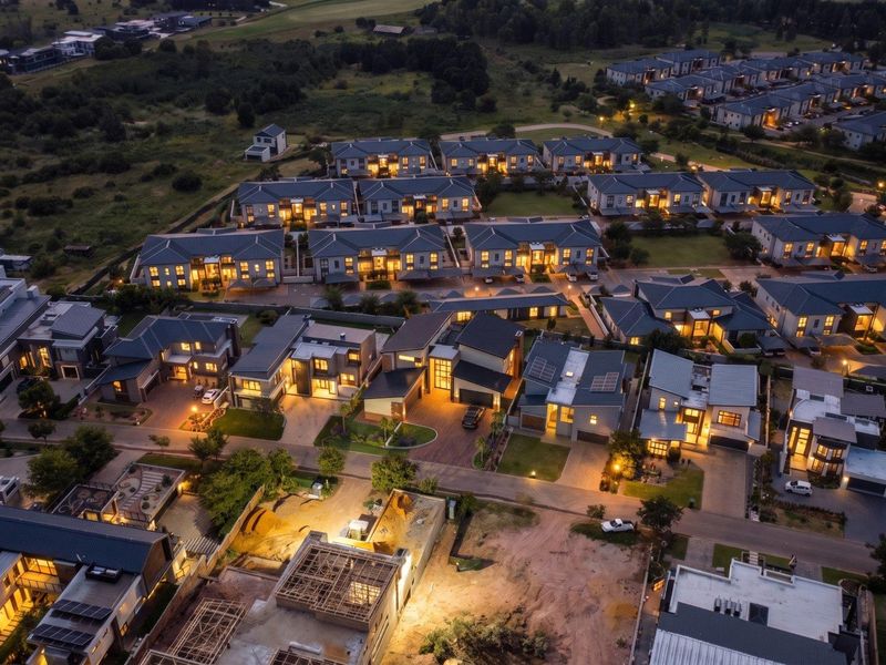 An elevated aerial view of a modern residential estate at night, showcasing multiple homes, paved streets, and integrated community lighting.