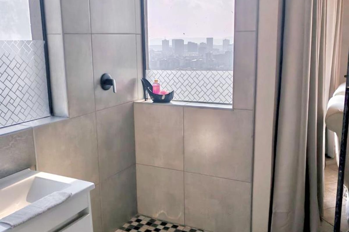 Modern bathroom featuring a walk-in shower with mosaic floor tiling, wall-mounted shower head, and a sleek vanity basin with a city view.