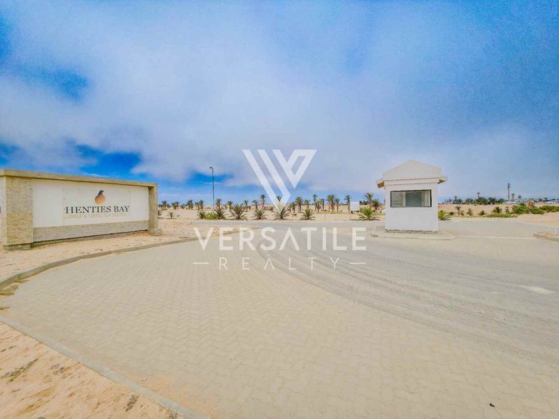 Entrance view of Henties Bay estate featuring a paved driveway, security gatehouse, and estate signage.