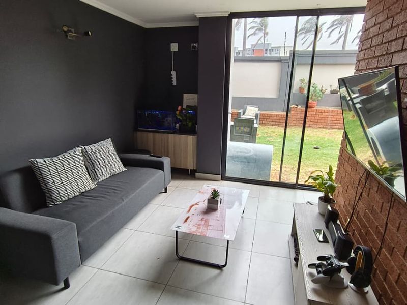 A modern living room featuring an exposed brick accent wall, large sliding glass doors providing natural light, and neutral tiled flooring.