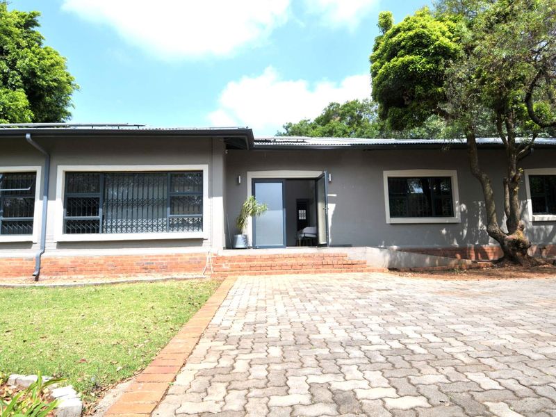 Front exterior view of a single-story commercial building featuring a paved driveway, brick foundation, and grey painted facade with secure aluminium windows.