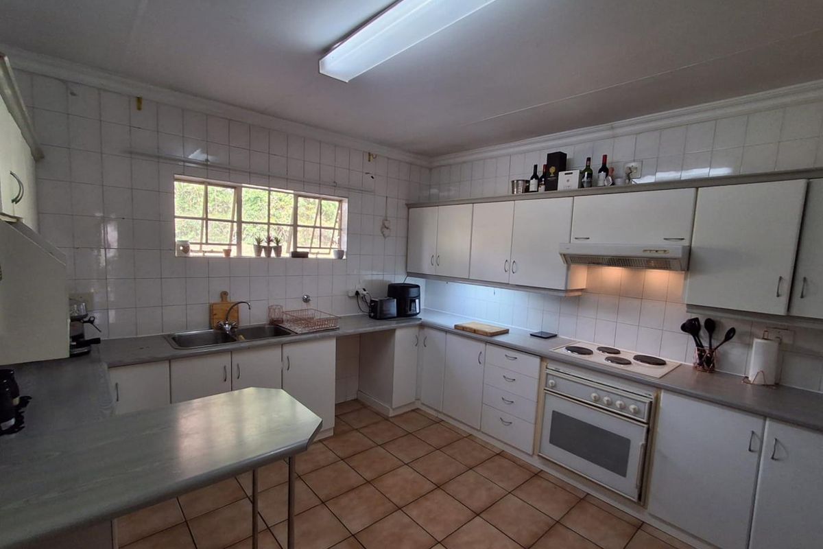 A functional kitchen featuring white cabinetry, tiled splashbacks, a built-in oven with hob, and a double sink with a breakfast nook area.
