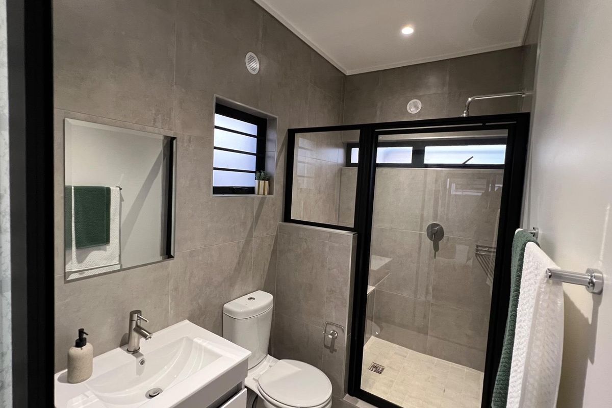 Modern bathroom featuring grey floor-to-ceiling tiles, a glass-enclosed walk-in shower with black framing, a vanity basin, and a toilet.