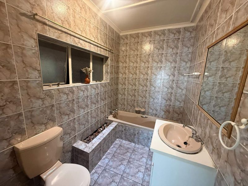 A functional bathroom featuring dated wall-to-wall tiling, a built-in bathtub, a vanity basin, and a standard toilet.