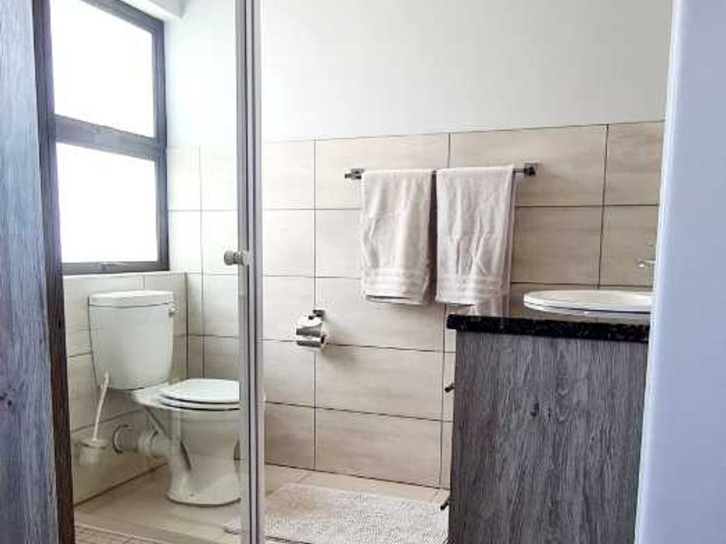 A functional bathroom featuring a shower enclosure, toilet, and vanity cabinet with tiled finishes throughout.