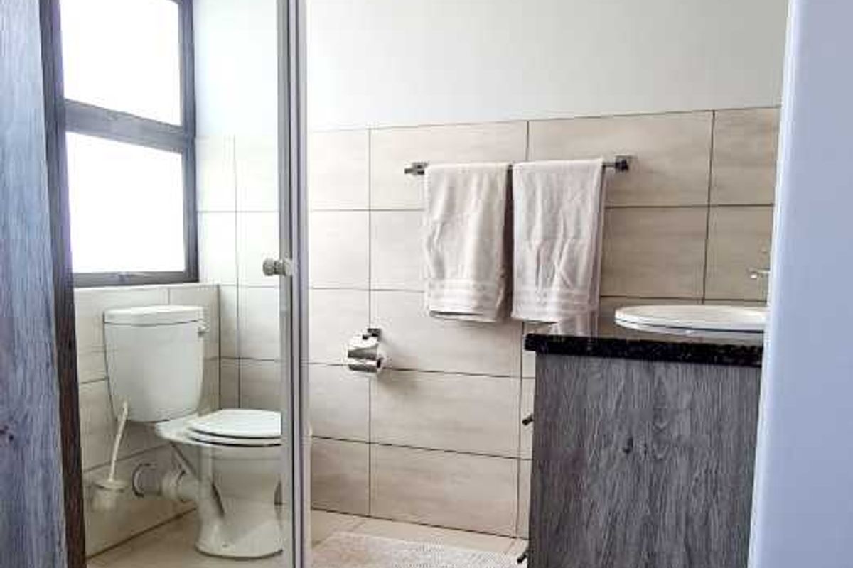 A functional bathroom featuring a shower enclosure, toilet, and vanity cabinet with tiled finishes throughout.