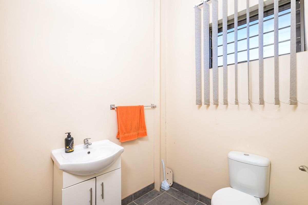 A functional bathroom featuring a vanity basin, toilet, and window with security bars and vertical blinds.