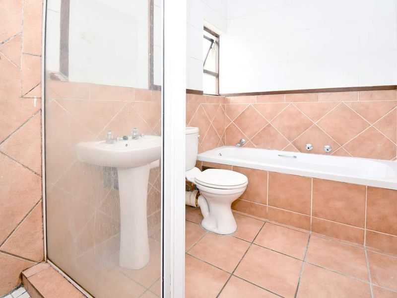 A functional bathroom featuring a pedestal basin, built-in bathtub, toilet, and a separate shower enclosure with tiled walls and flooring.