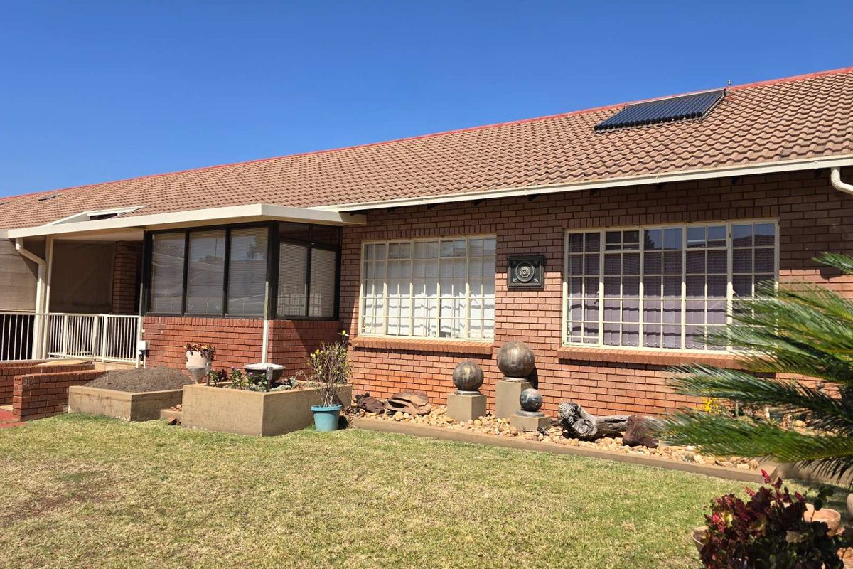 A well-maintained brick house exterior featuring a tiled roof, solar water heating panel, and a covered patio area overlooking the garden.
