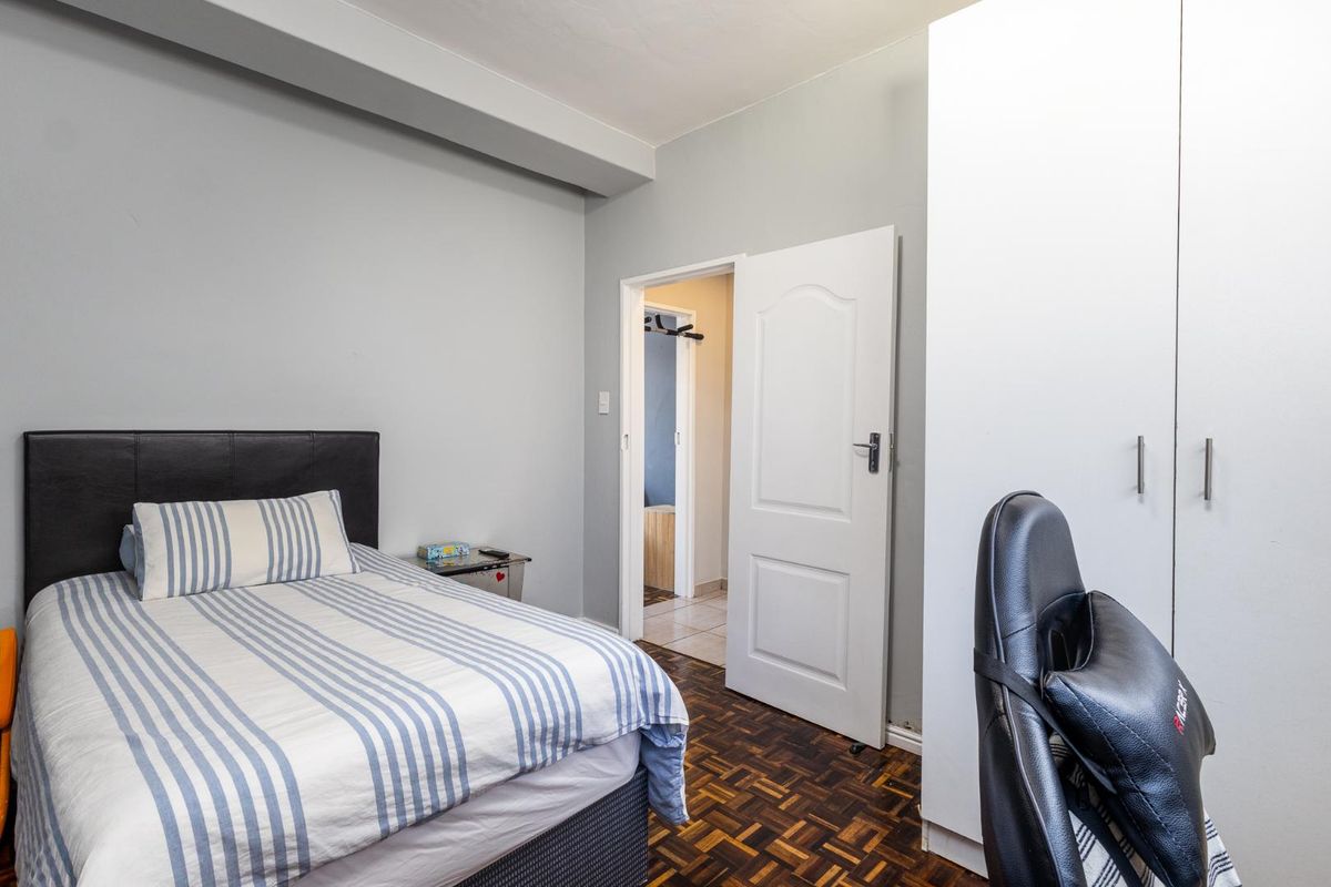 A bedroom featuring parquet flooring, built-in cupboards, and an adjoining doorway leading to a secondary space.