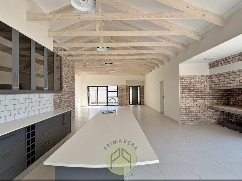 Spacious open-plan living area featuring exposed timber trusses, brick feature walls, a modern kitchen island, and a built-in fireplace.