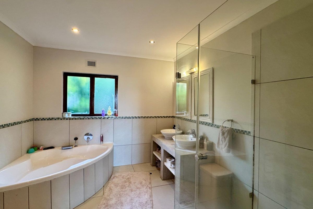 A well-appointed bathroom featuring a corner bathtub, a double vanity with vessel sinks, and a spacious glass-enclosed shower with modern tiling.
