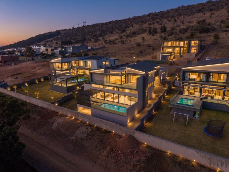 An elevated aerial view of modern residential properties featuring contemporary architecture, private swimming pools, balconies, and integrated outdoor lighting at dusk.