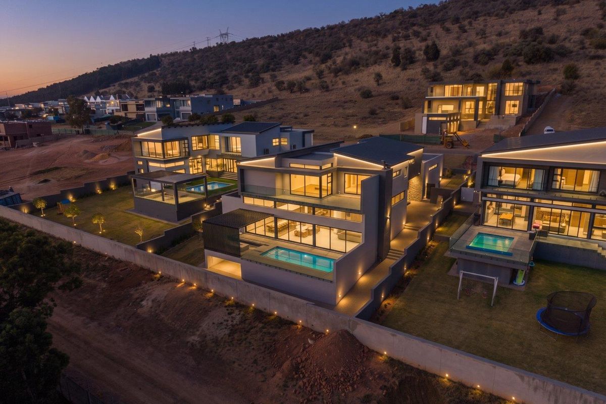 An elevated aerial view of modern residential properties featuring contemporary architecture, private swimming pools, balconies, and integrated outdoor lighting at dusk.