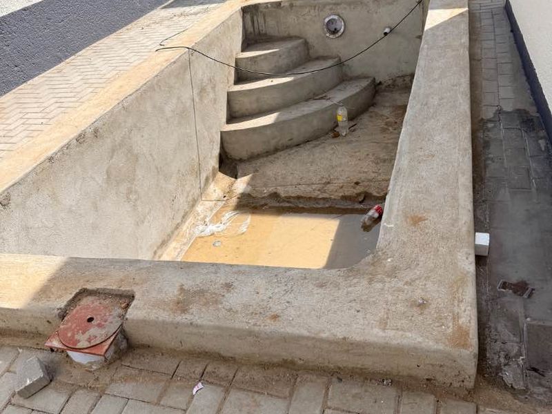 An unfinished concrete swimming pool structure featuring integrated steps, currently under construction with surrounding paving.