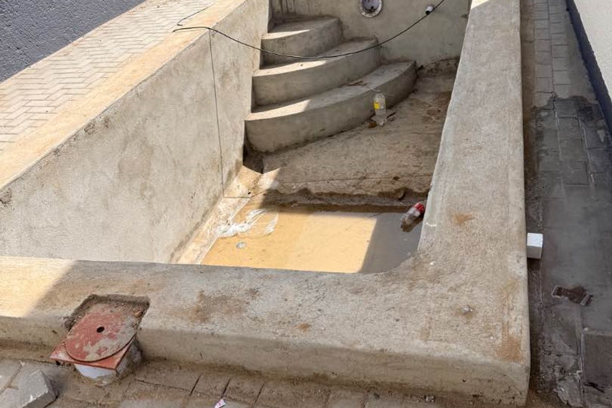 An unfinished concrete swimming pool structure featuring integrated steps, currently under construction with surrounding paving.