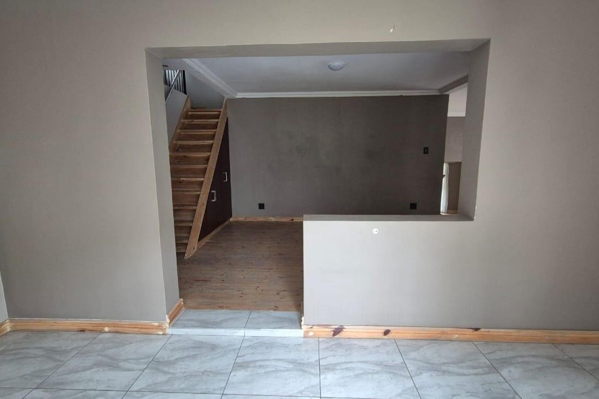 An empty living area featuring a wooden staircase, tiled flooring, and a large pass-through opening connecting to an adjacent space.