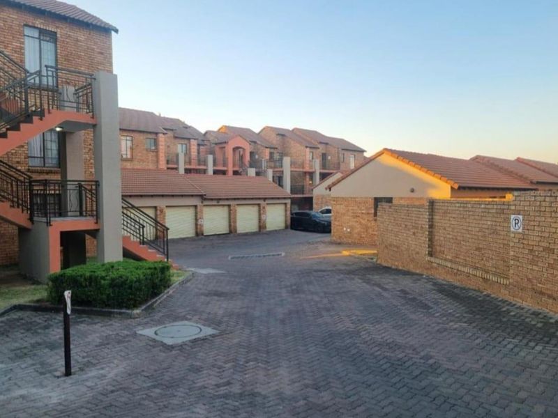 Exterior view of an apartment complex featuring brick buildings, a paved driveway, and a row of garage units.