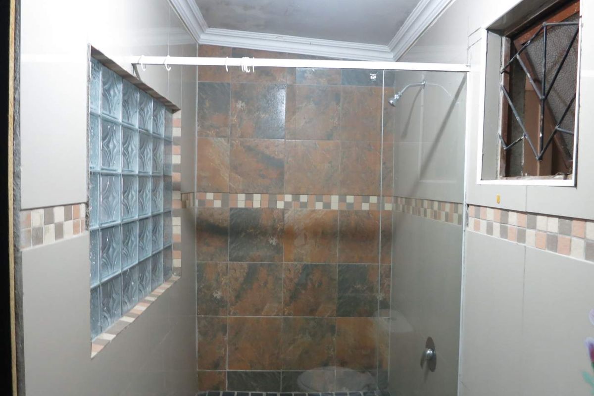 A walk-in shower featuring slate-style wall tiles, a glass partition, glass block feature window, and a small high-level window with security bars.